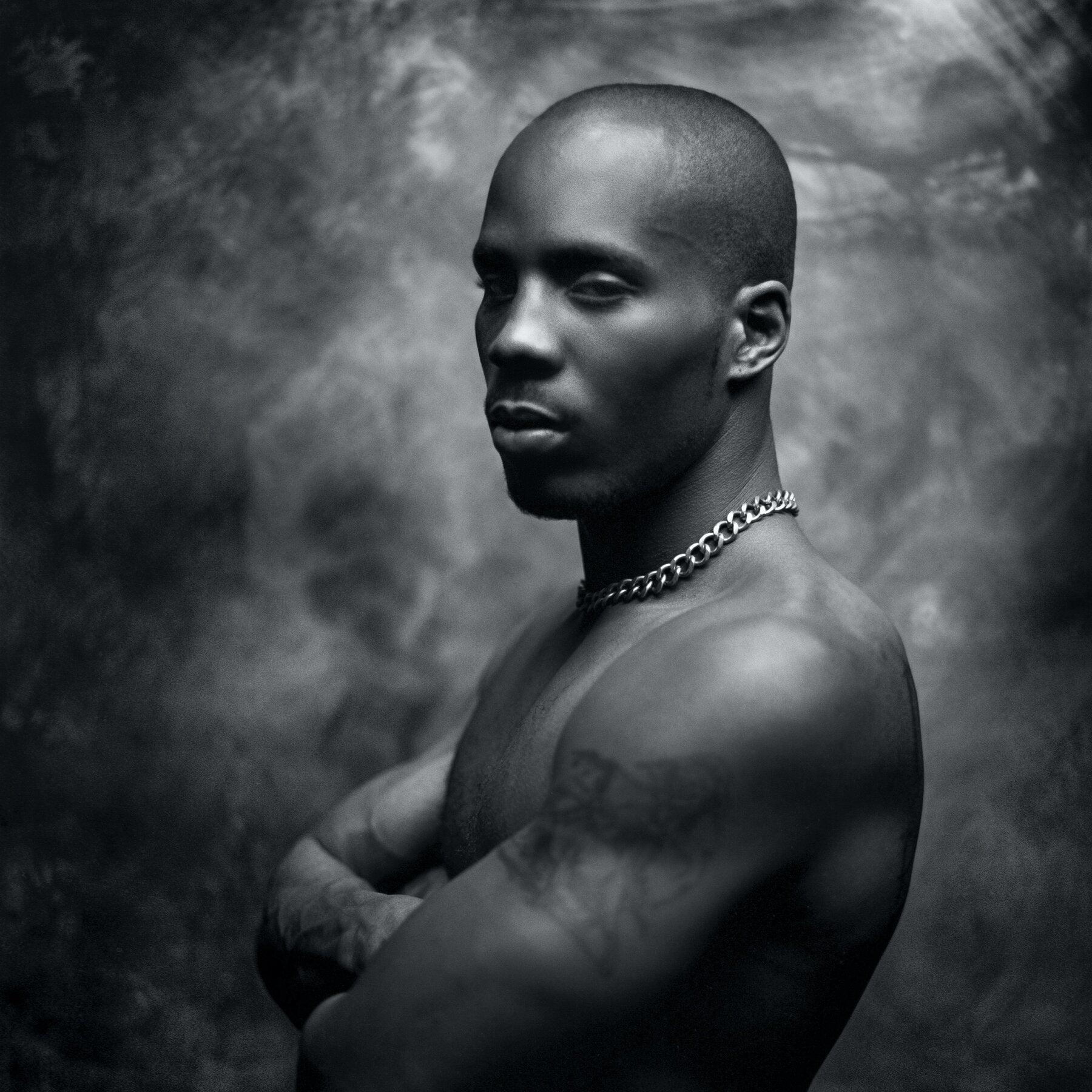Black and white portrait of a shirtless man with a chain necklace against a textured dark background