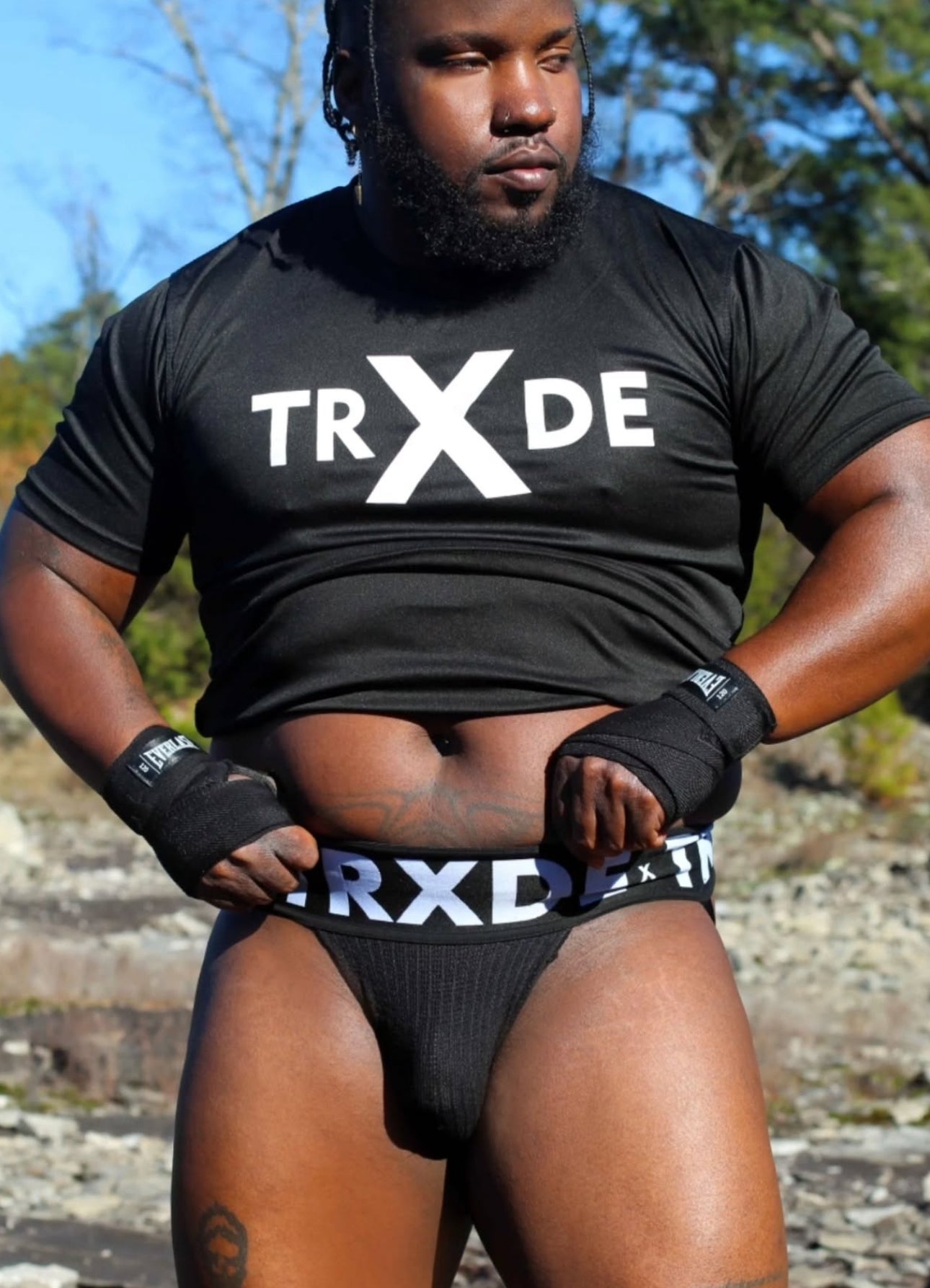 Person wearing a black 'TRXDE' t-shirt and underwear outdoors.