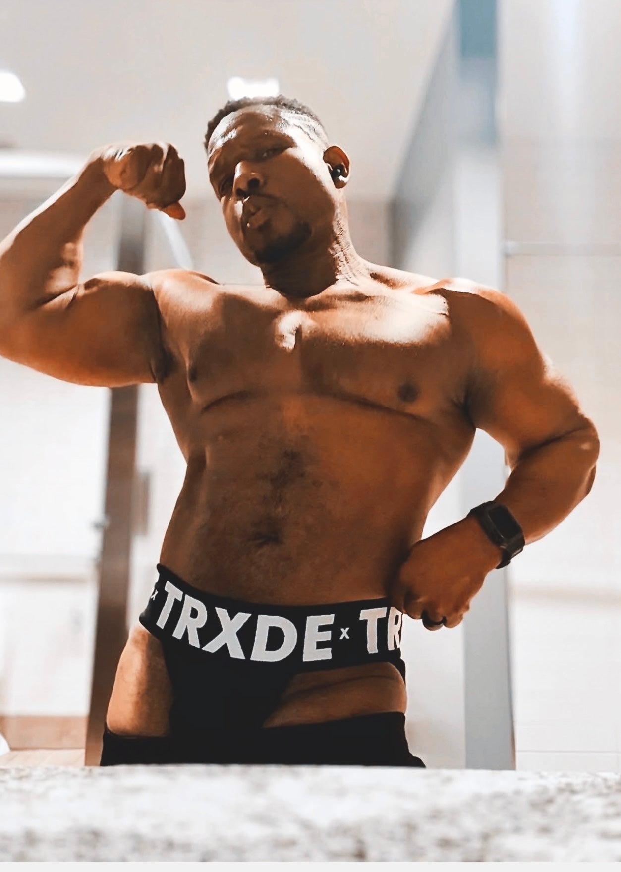 Muscular man flexing his arm wearing TRXDE underwear in a bright indoor setting
