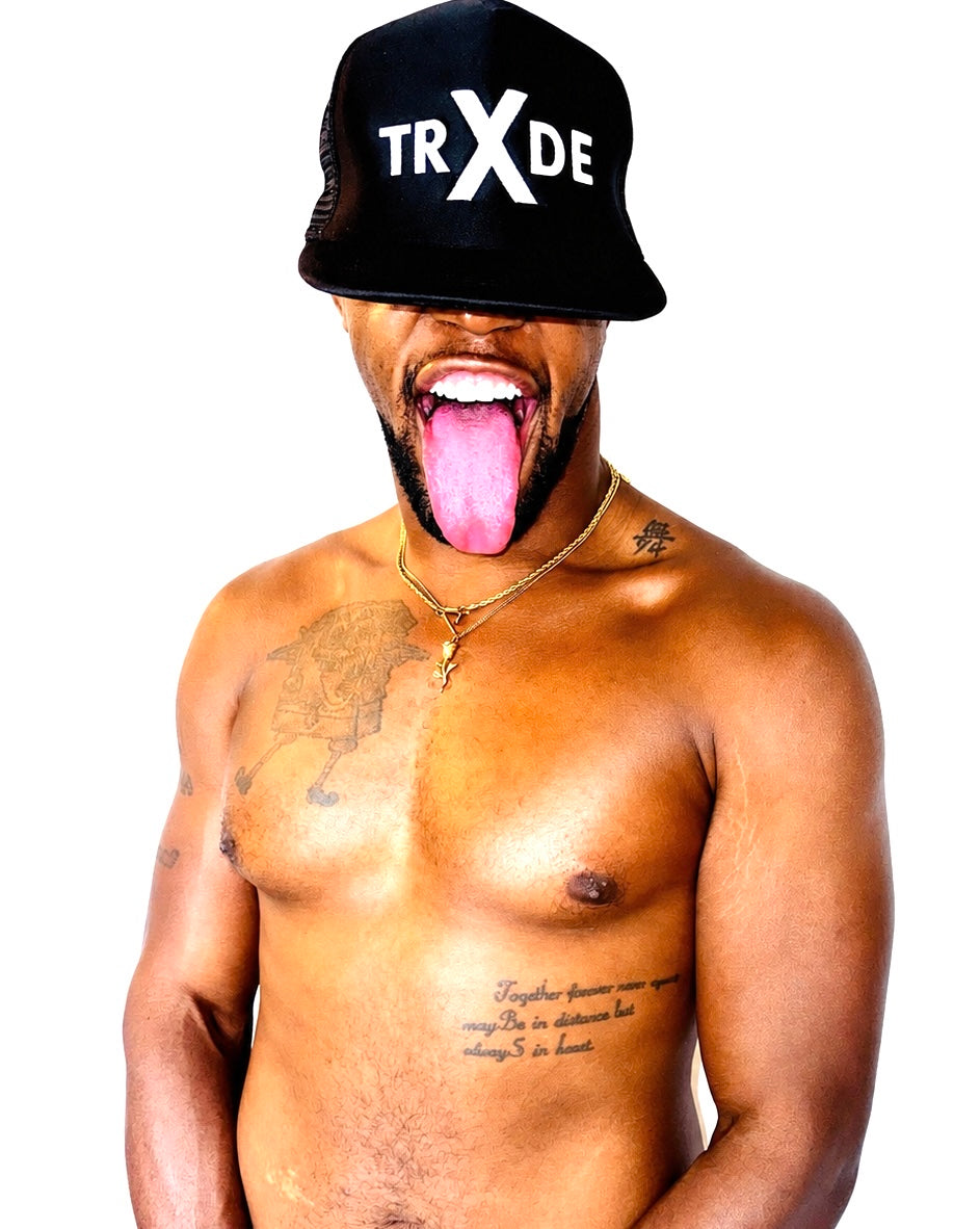 A shirtless man with tattoos wearing a black mesh bucket hat with 'TRXDE' in white text, sticking his tongue out against a white background.
