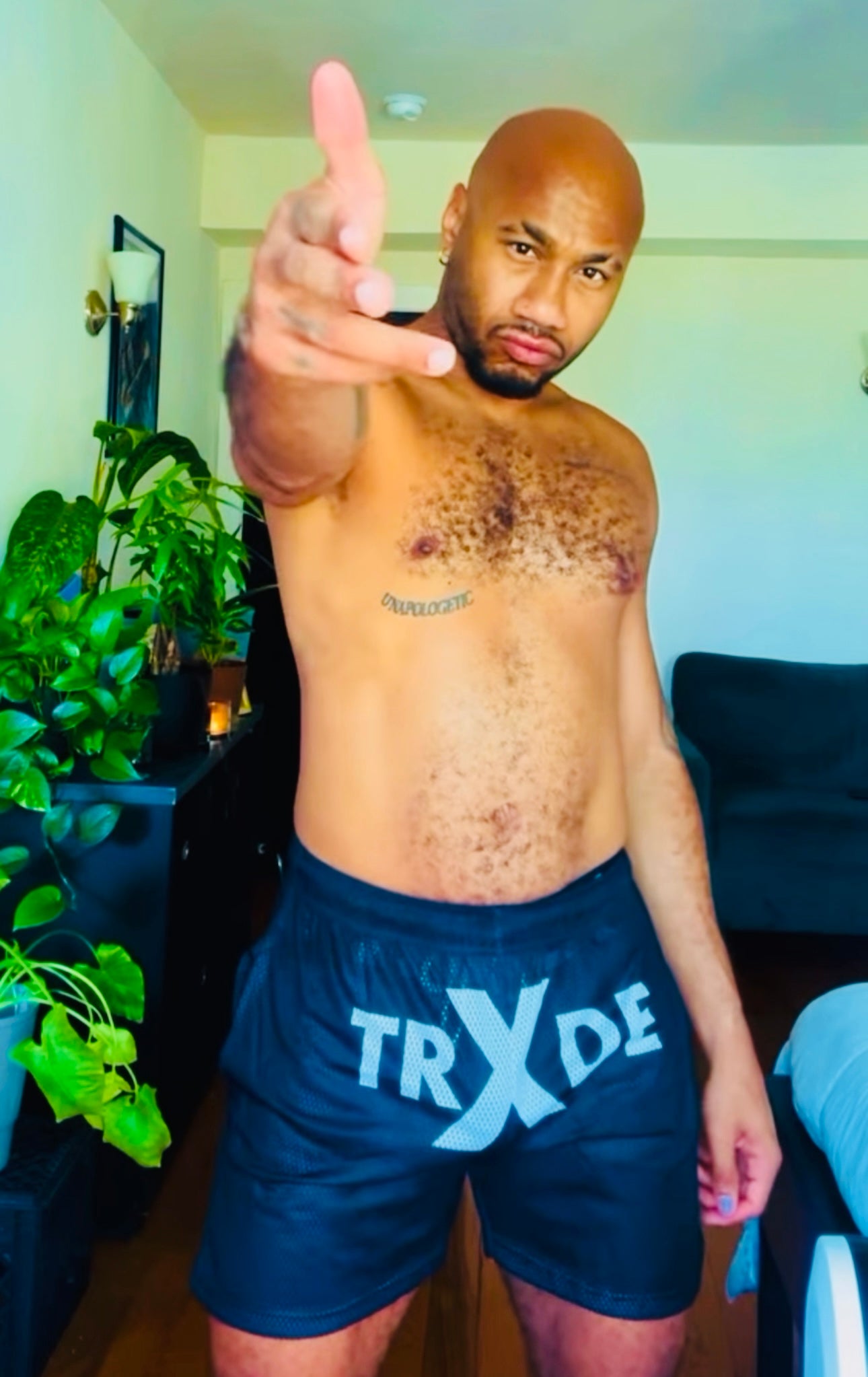 Man wearing blue shorts with 'TRXDE' branding, pointing forward indoors.
