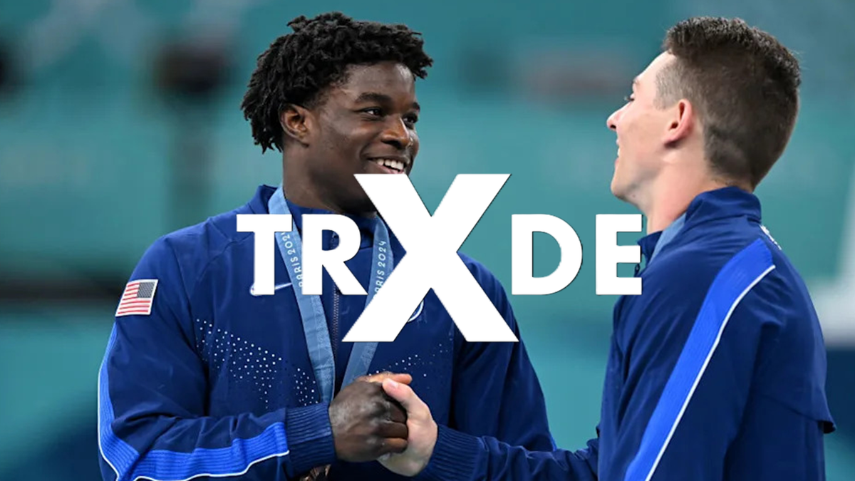 Two athletes in blue athletic jackets shaking hands on a podium, with a large white 'TRX' logo overlay across the center.